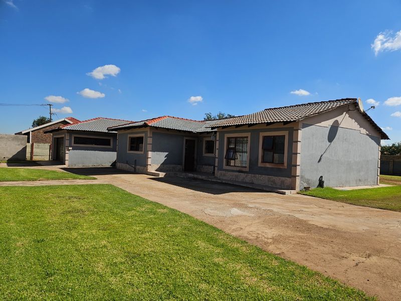 Front exterior view of a single-story house featuring a tiled roof, concrete driveway, and attached garage with a surrounding lawn.