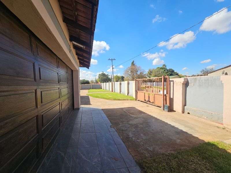 Front exterior view featuring a garage, tiled walkway, concrete driveway, and perimeter wall with a metal gate.