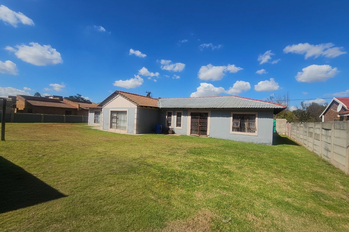 Rear view of a single-story residential house featuring a tiled roof, security gates, and a spacious surrounding lawn with perimeter walling.