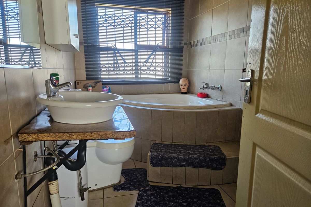 A dated bathroom featuring a corner bathtub, vessel sink with exposed plumbing, and tiled finishes throughout.