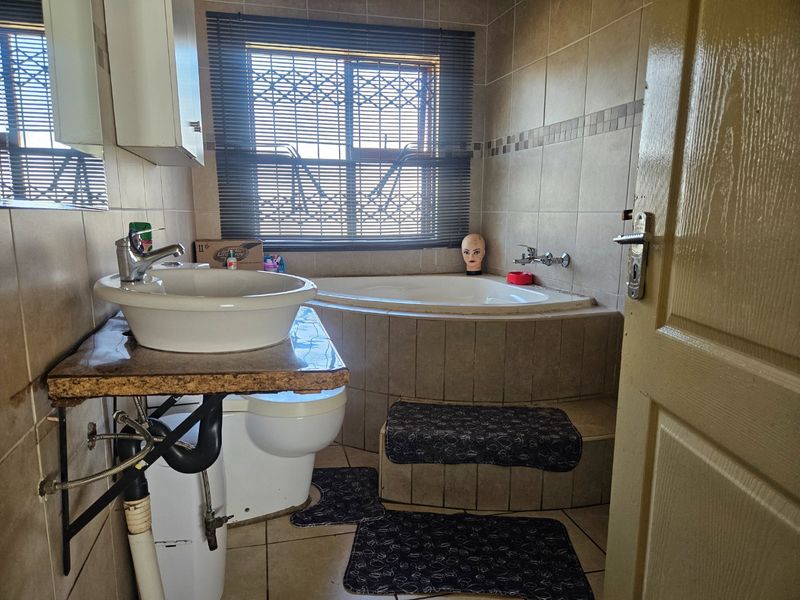 A dated bathroom featuring a corner bathtub, vessel sink with exposed plumbing, and tiled finishes throughout.