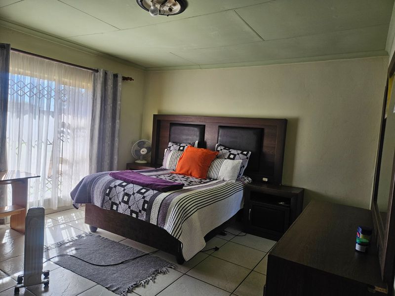 A bedroom featuring tiled flooring and a sliding glass door with security gate, providing access to the exterior.