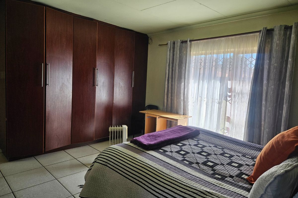 A bedroom featuring tiled flooring and extensive built-in wooden cupboards, providing ample storage space and natural light through the window.