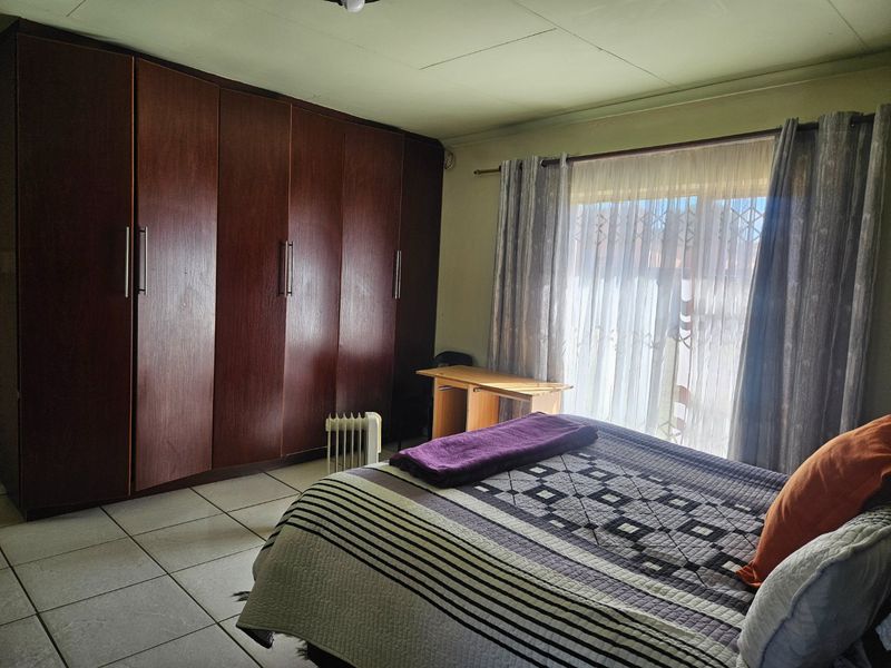 A bedroom featuring tiled flooring and extensive built-in wooden cupboards, providing ample storage space and natural light through the window.
