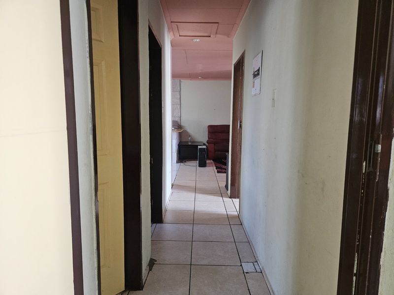 A functional hallway with tiled flooring and multiple internal doors, leading towards an open living area with a pink-painted ceiling.