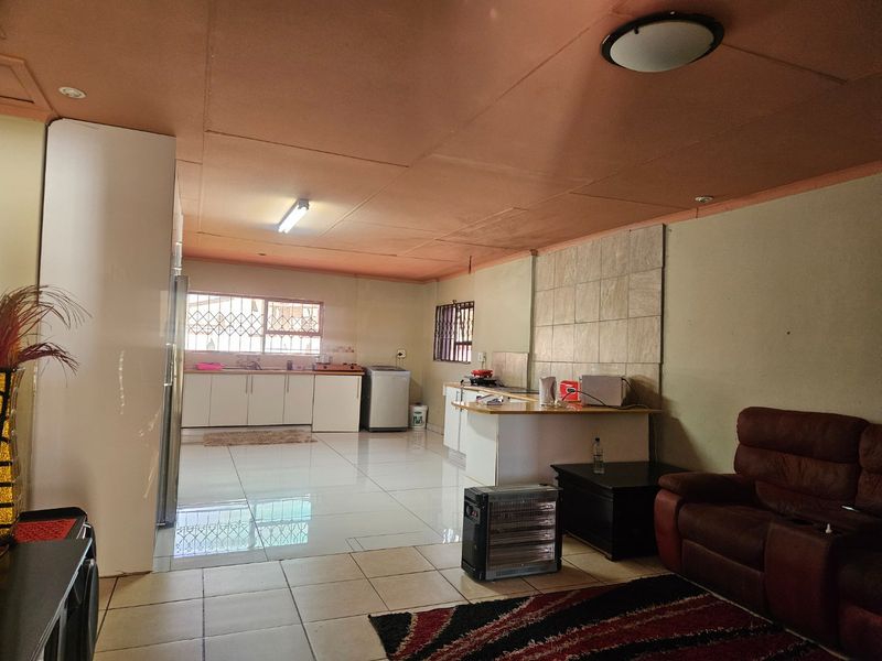 Open-plan living and kitchen area featuring tiled flooring, built-in cabinetry, and security bars on windows, offering a functional layout with potential for modernization.