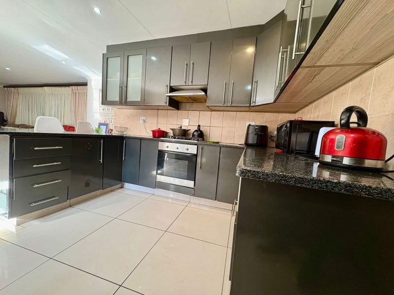 Modern kitchen featuring dark grey cabinetry, granite countertops, built-in oven with gas hob, extractor fan, and neutral tiled flooring.