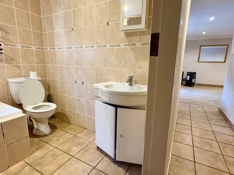 A dated bathroom featuring ceramic tiling, a pedestal vanity, and a bathtub, requiring cosmetic updates to modernize the space.