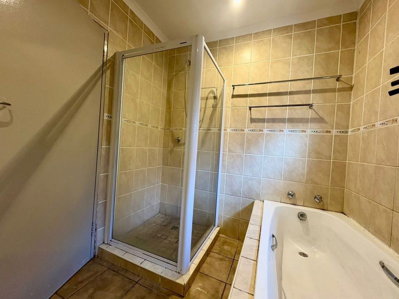 A functional bathroom featuring a separate shower enclosure, a built-in bathtub, and neutral ceramic wall and floor tiling.