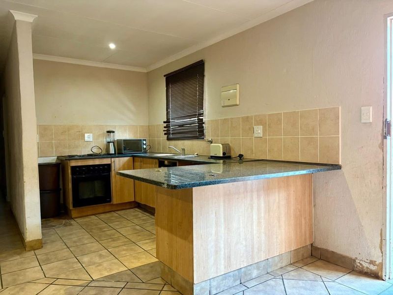 Functional kitchen featuring wood-finish cabinetry, granite countertops, ceramic tile backsplash, and a breakfast bar, with tiled flooring throughout.