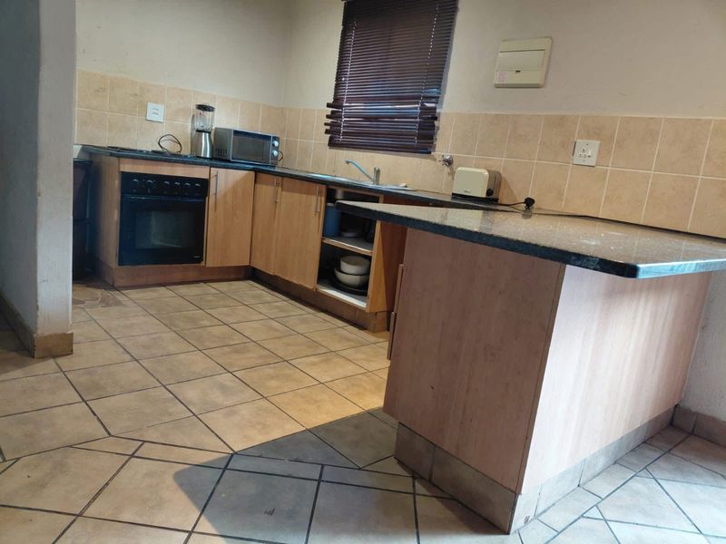 Functional kitchen featuring granite countertops, built-in oven, hob, and tiled flooring. The space offers practical cabinetry and a breakfast counter layout.