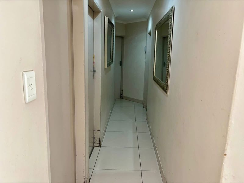 A narrow residential hallway featuring tiled flooring and recessed lighting, providing access to multiple internal rooms.