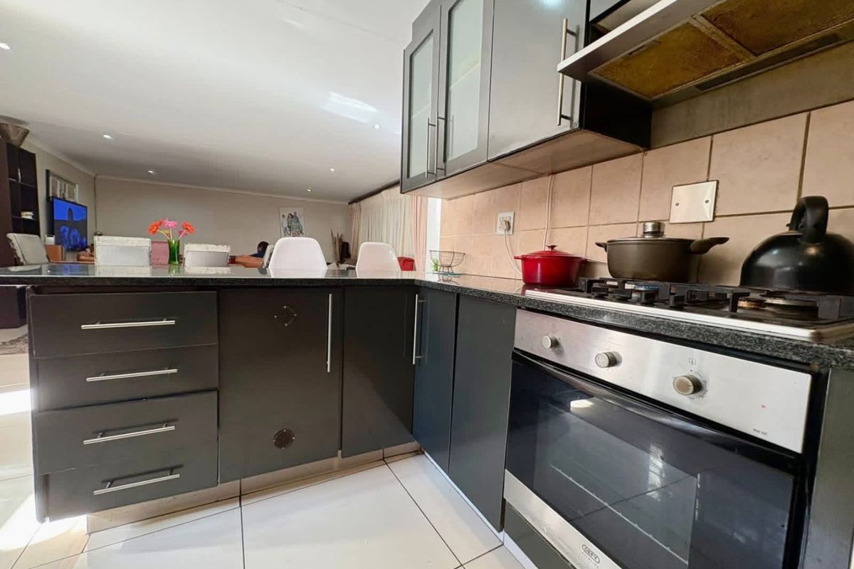 Modern kitchen featuring dark cabinetry, granite countertops, gas hob, built-in oven, and extractor fan, flowing into an open-plan living area.