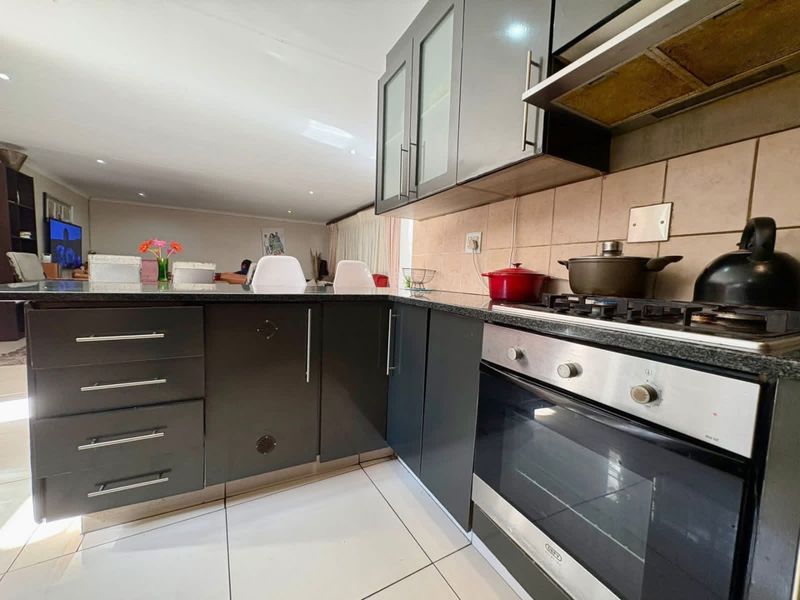 Modern kitchen featuring dark cabinetry, granite countertops, gas hob, built-in oven, and extractor fan, flowing into an open-plan living area.