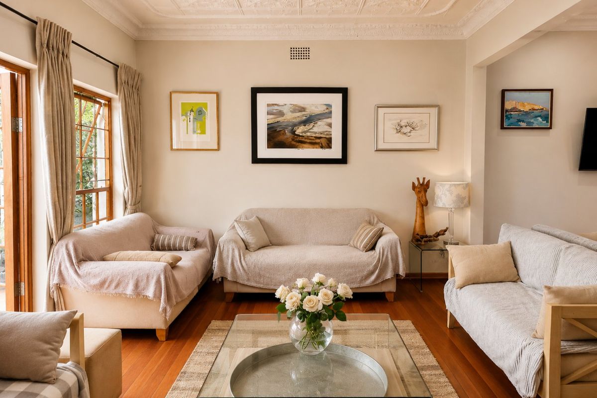 A well-maintained living room featuring polished hardwood floors, an ornate coffered ceiling, and natural light through timber-framed windows and doors.