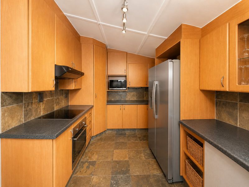 A functional kitchen featuring wood-tone cabinetry, dark laminate countertops, slate-style floor tiles, and integrated appliances including an oven, cooktop, and microwave.