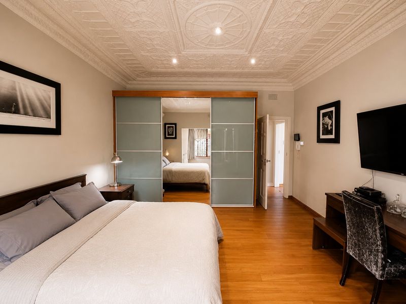 Spacious bedroom featuring hardwood flooring, an ornate plaster ceiling with recessed lighting, and modern sliding glass wardrobe doors.