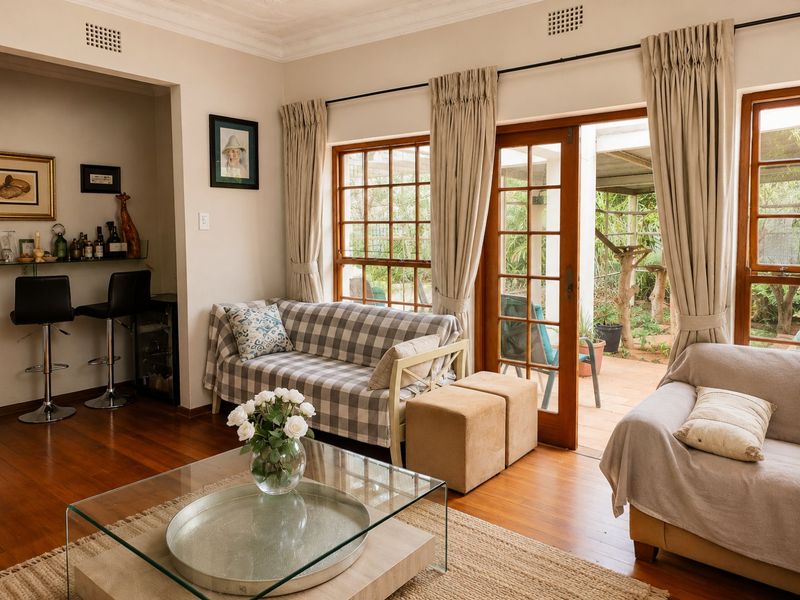 A bright living room featuring hardwood floors, timber-framed doors opening to a patio, and a dedicated built-in bar area.