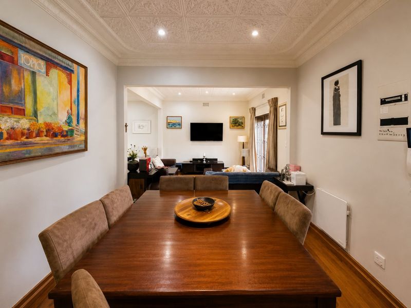 An open-plan dining and living area featuring decorative ceiling detailing, hardwood flooring, and recessed lighting, creating a cohesive and well-maintained living space.