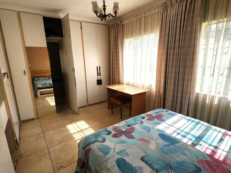 A bedroom featuring tiled flooring, built-in cupboards with a mirrored section, and natural light through large windows.