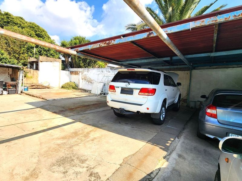 Outdoor carport area with a concrete driveway and perimeter boundary walls, showing significant signs of weathering and corrosion on the metal structure.