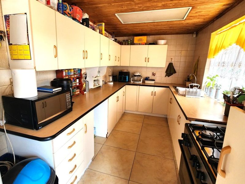 A functional kitchen featuring laminate cabinetry, tiled flooring, a timber ceiling, and a gas stove, offering potential for a modern renovation.