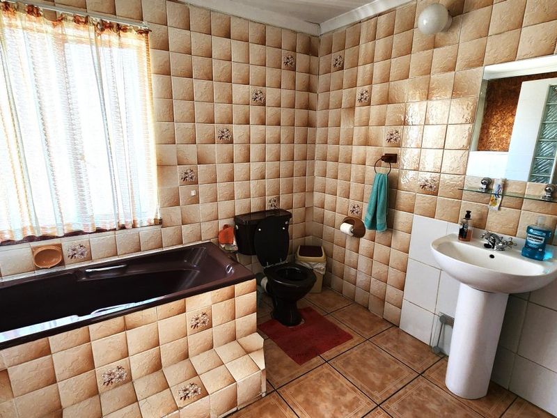A dated bathroom featuring a pedestal basin, built-in bathtub, and toilet, finished with traditional wall and floor tiling throughout.