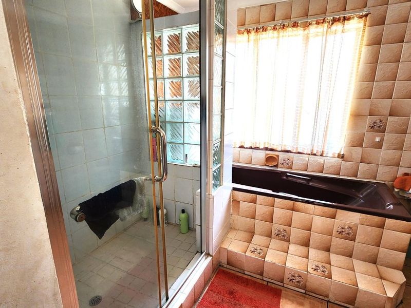 A dated bathroom featuring a built-in bathtub with tiled surround, a separate glass-enclosed shower, and glass block window detailing.