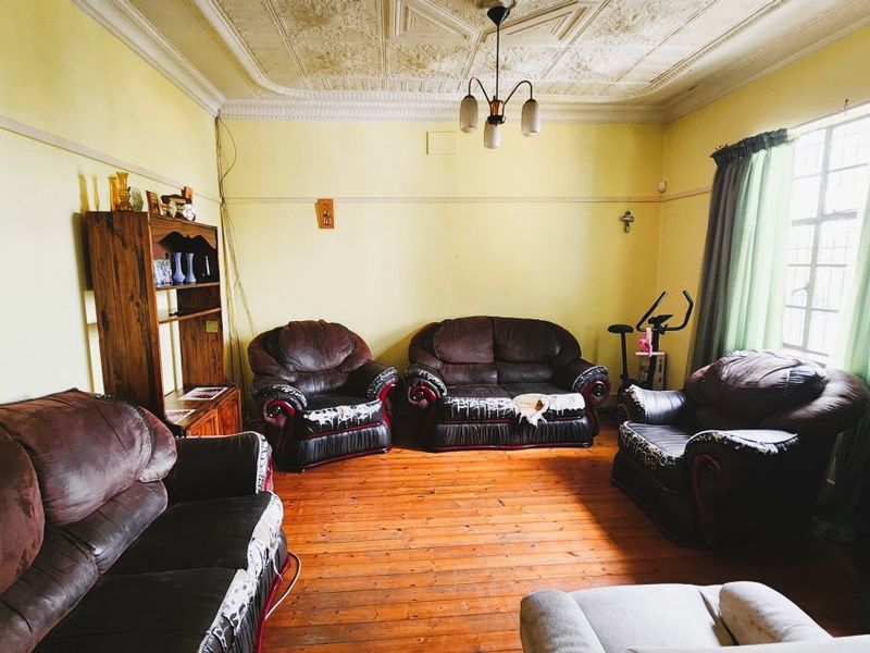 A spacious living room featuring original ornate pressed metal ceilings, hardwood timber flooring, and classic picture rails, offering a character-filled foundation for renovation.