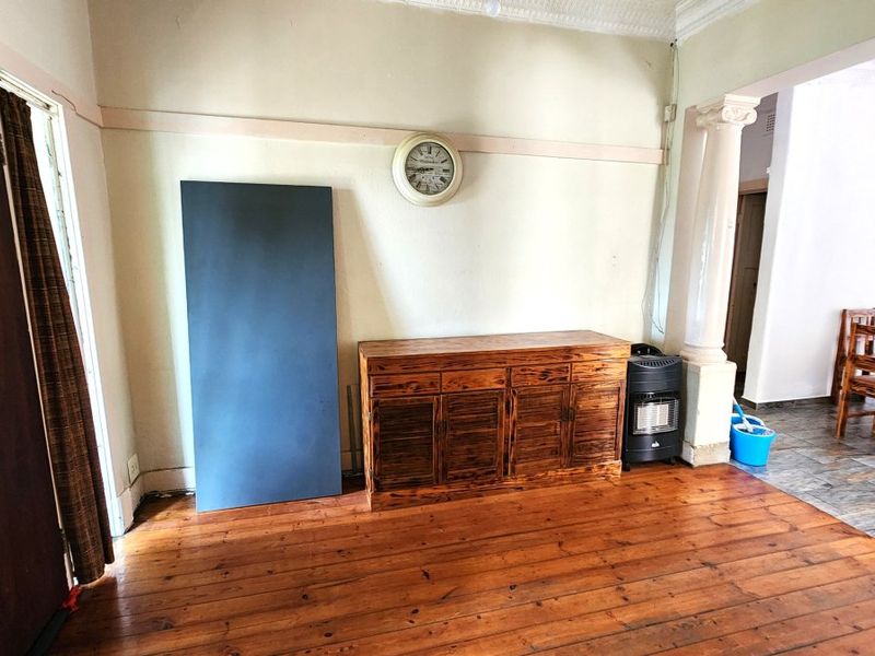 Living area featuring original hardwood flooring, decorative ceiling cornices, and a classical column, offering a character-filled space with potential for modernization.
