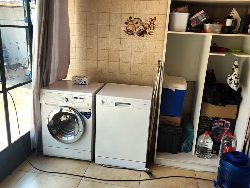 A functional laundry area featuring tiled splashbacks, built-in storage shelving, and direct access to the exterior via a security gate.