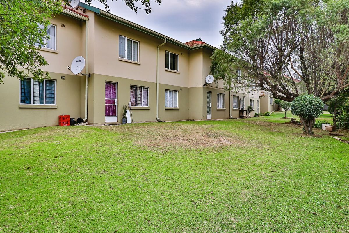 Rear view of the apartment complex featuring a shared lawn area, established trees, and exterior building facade with satellite dishes.