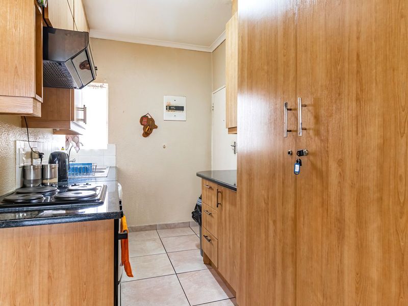 A functional kitchen featuring wood-look laminate cabinetry, black granite countertops, an electric hob with extractor fan, and tiled flooring.