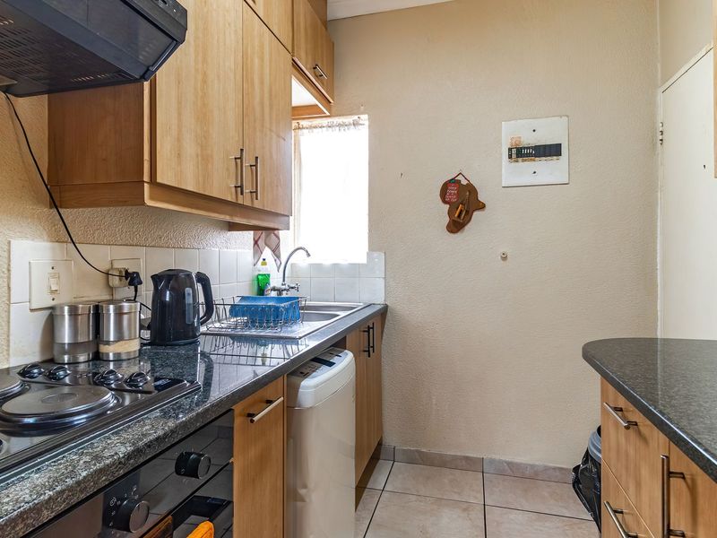 Compact kitchen featuring wooden cabinetry, dark laminate countertops, built-in electric hob and oven, and tiled flooring.