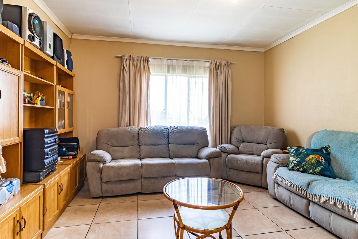 A living room featuring tiled flooring, a large window, and a built-in wooden shelving unit.
