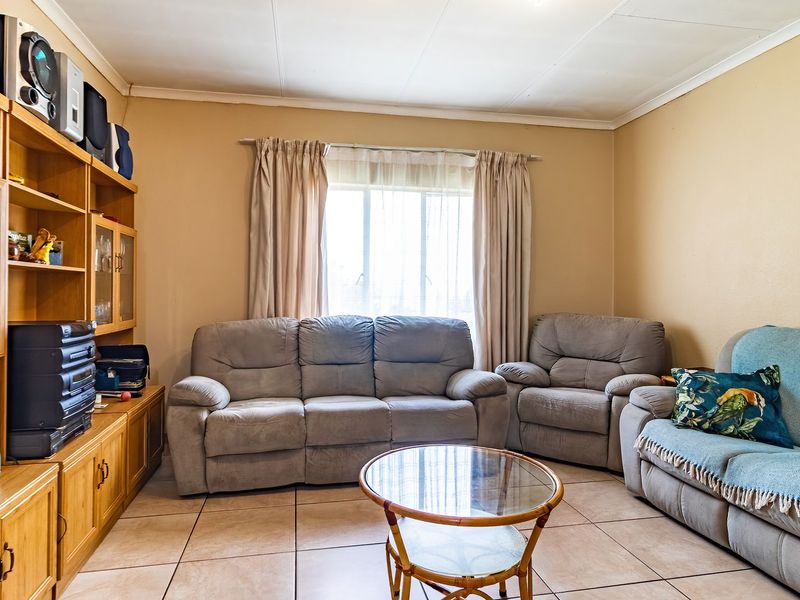 A living room featuring tiled flooring, a large window, and a built-in wooden shelving unit.