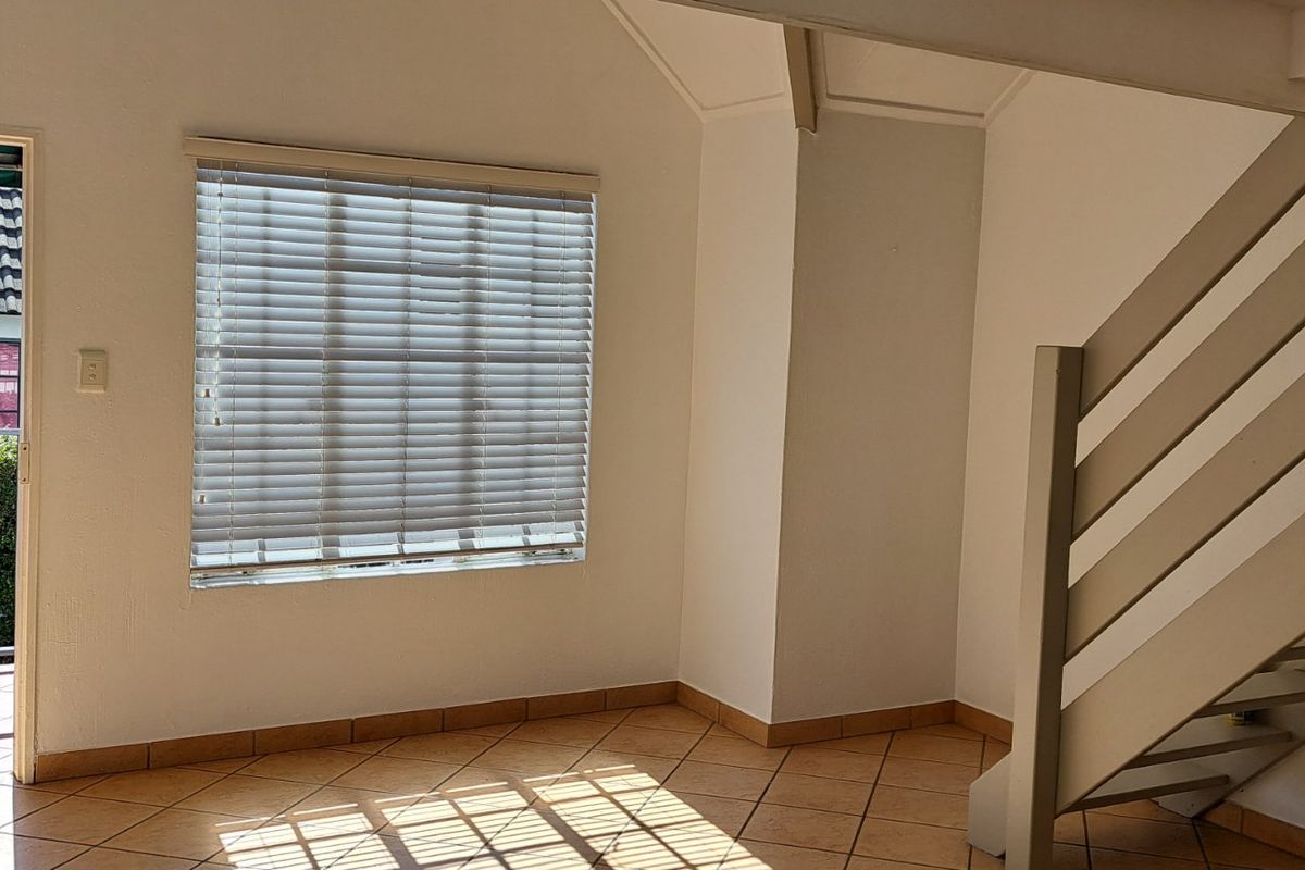 An open-plan living area featuring tiled flooring, a staircase leading to an upper level, and direct access to a balcony through a door.