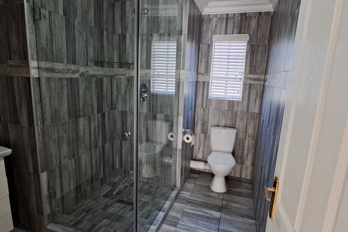 Modern bathroom featuring a glass-enclosed shower, wall-mounted vanity, and floor-to-ceiling grey wood-look tiling.