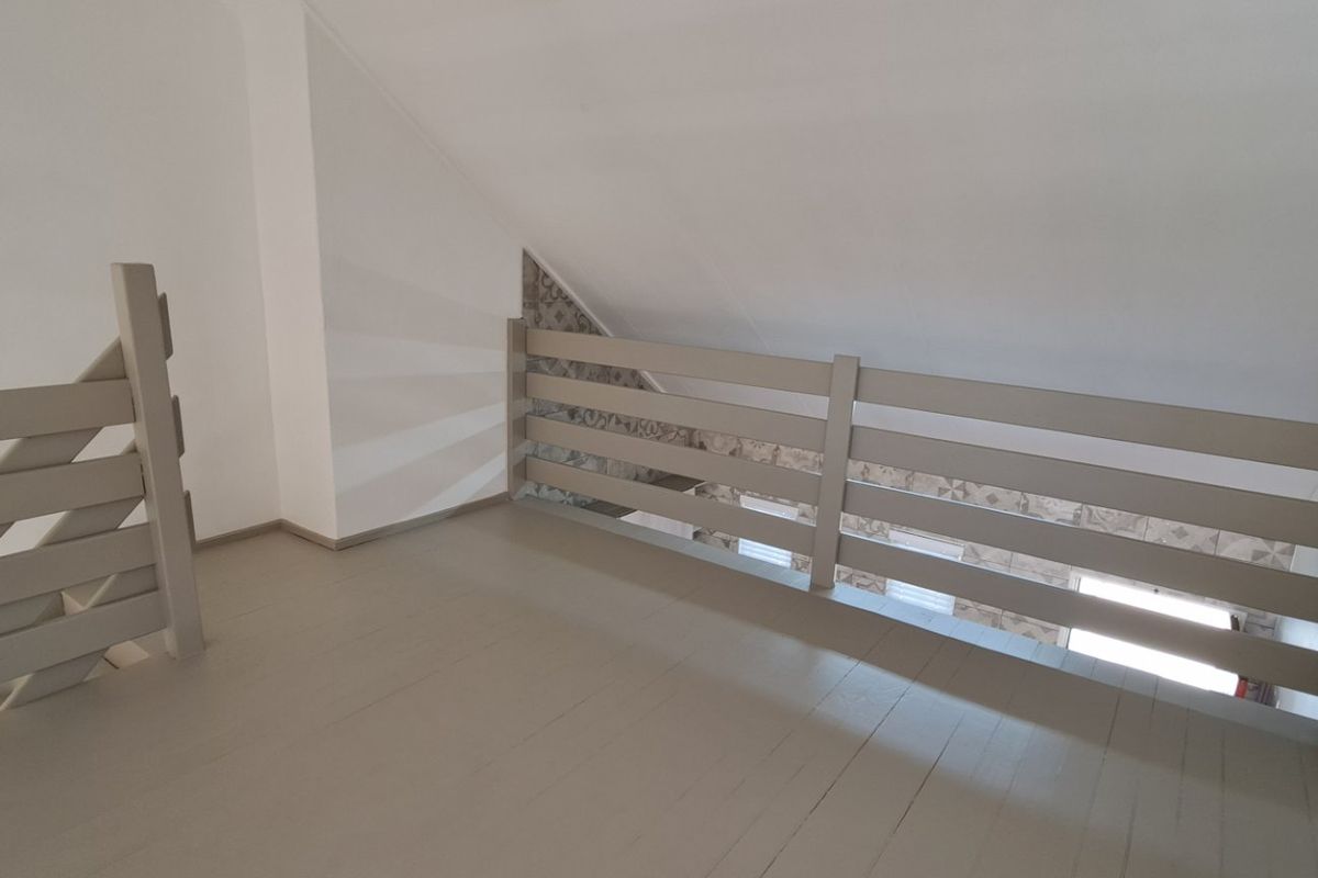 An empty loft-style bedroom area featuring a sloped ceiling, timber flooring, and a protective timber balustrade overlooking the lower level.