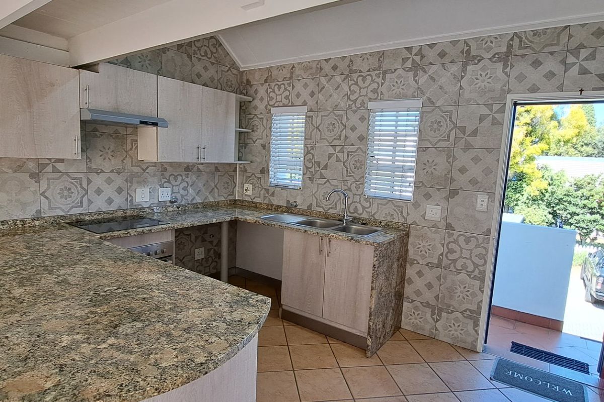A functional kitchen featuring granite countertops, ample cabinetry, a double sink, and a tiled backsplash, with direct access to an outdoor area.