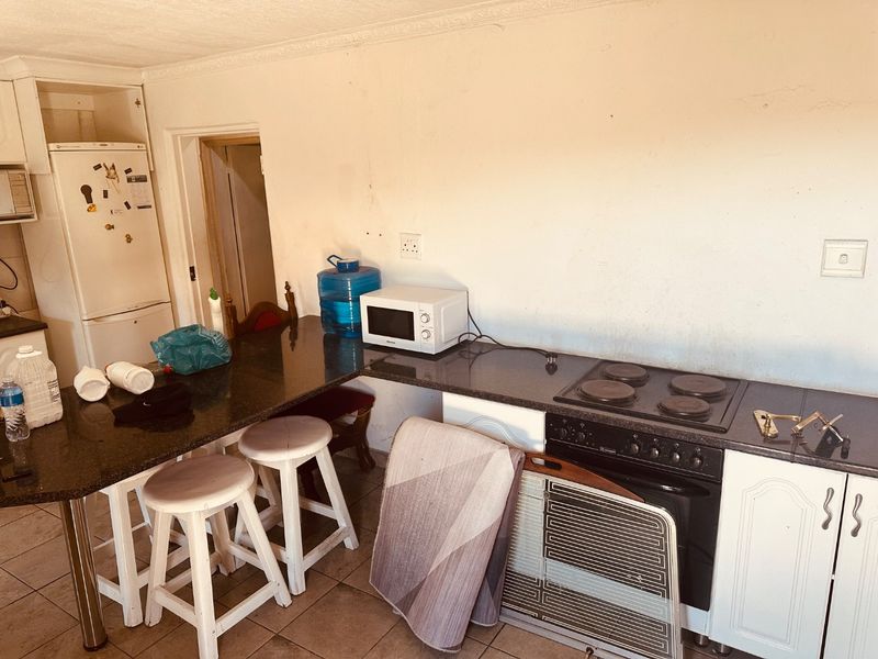 A functional kitchen featuring granite countertops, built-in oven and hob, and tiled flooring, offering a practical layout with potential for cosmetic updates.