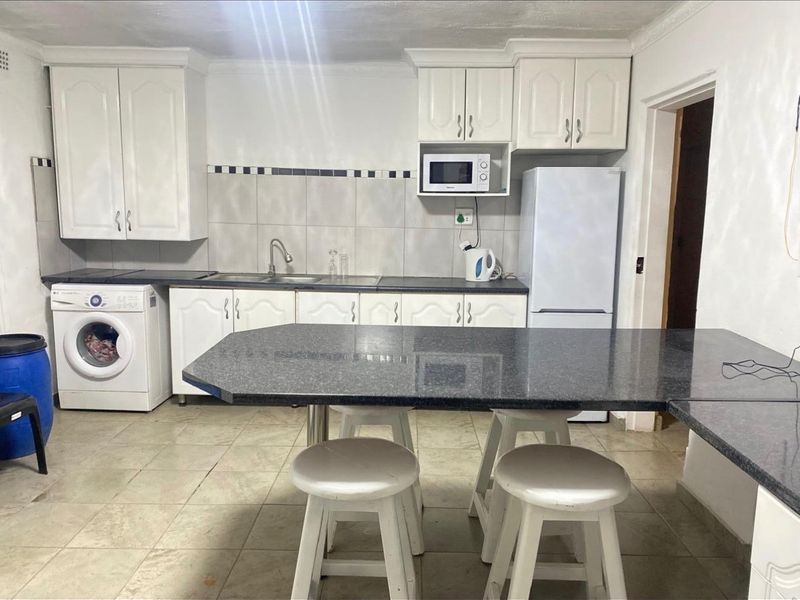 Functional kitchen featuring white cabinetry, dark laminate countertops, tiled backsplash, and integrated laundry space, offering a practical layout for daily use.
