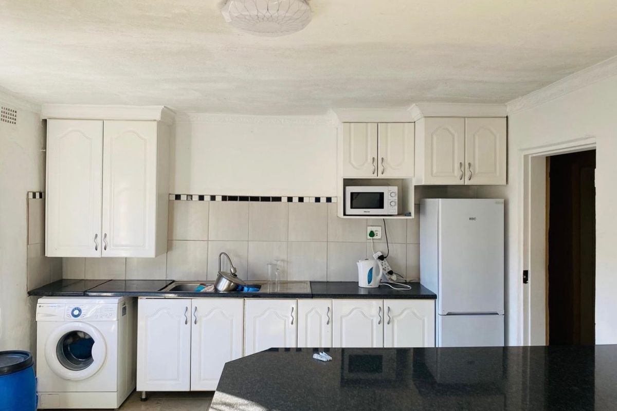 A functional kitchen featuring white cabinetry, dark countertops, a tiled backsplash, and integrated appliance space, offering a practical layout for daily use.
