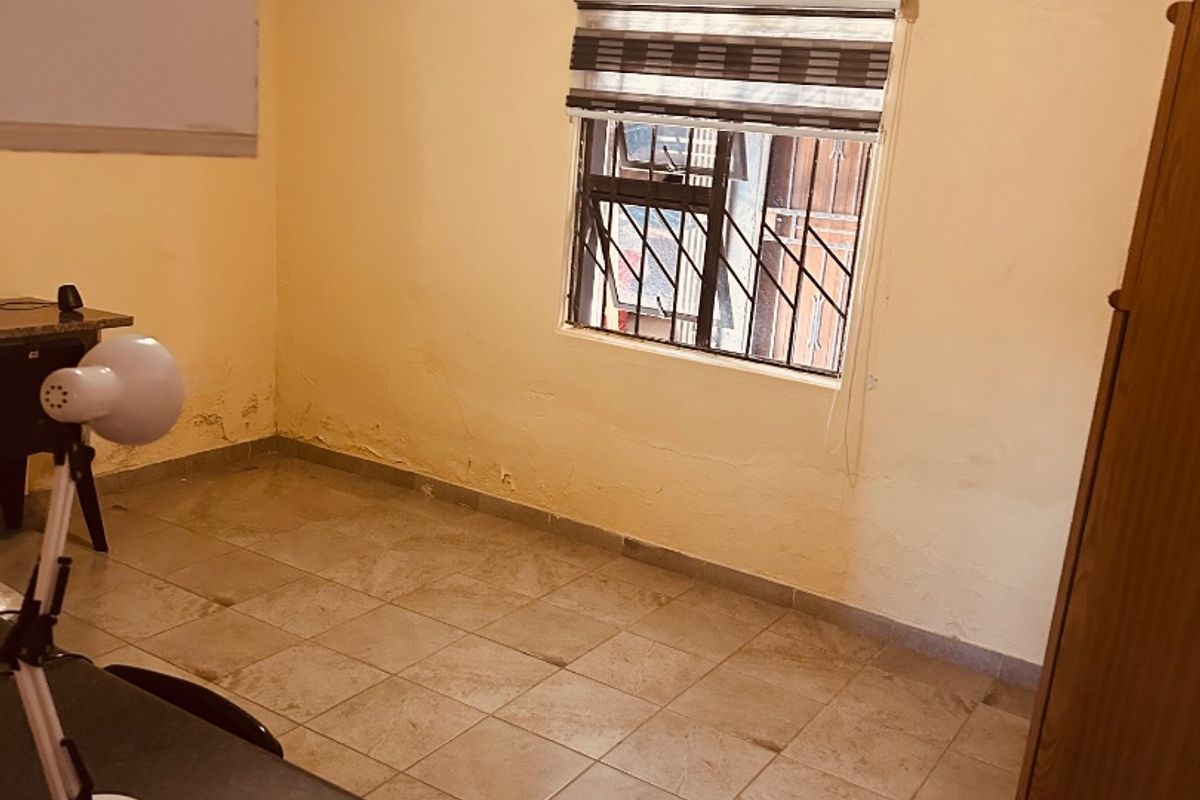 A bedroom featuring tiled flooring, security bars on the window, and a roller blind. The walls show signs of wear and potential damp damage.