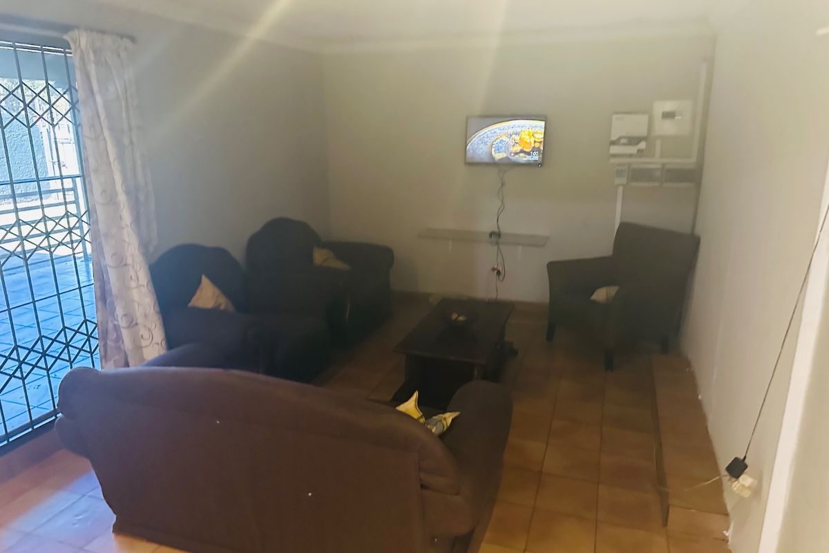 A living room featuring tiled flooring and a security gate, with visible electrical infrastructure and wall imperfections.
