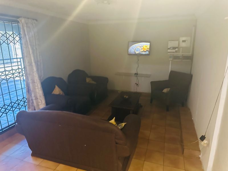 A living room featuring tiled flooring and a security gate, with visible electrical infrastructure and wall imperfections.