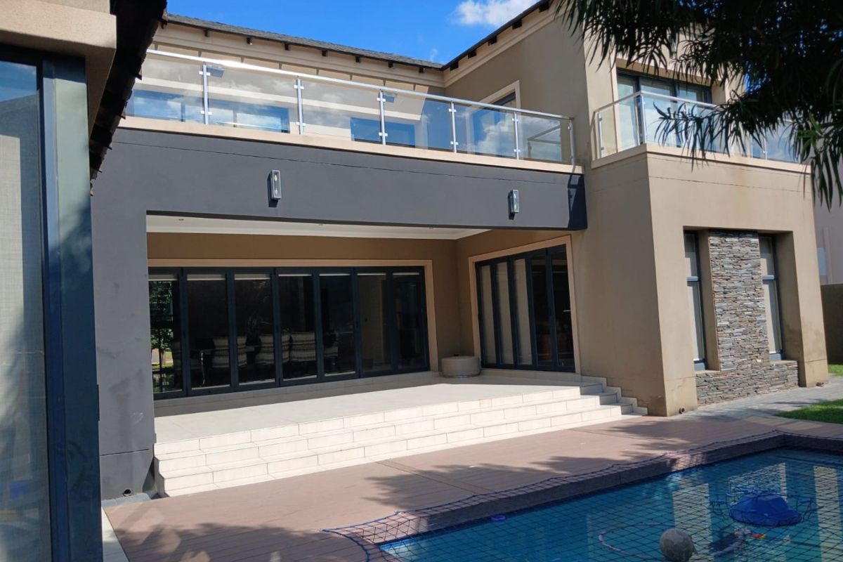 Rear elevation featuring a modern swimming pool, expansive tiled patio, stacked folding doors, and an upper-level balcony with a glass balustrade.