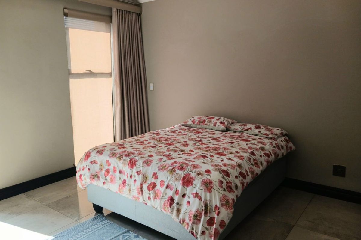 A well-lit bedroom featuring neutral wall tones, tiled flooring, and large windows with installed curtain tracks.