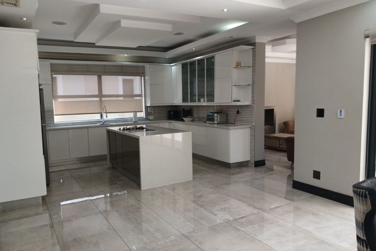 Modern kitchen featuring a central island, sleek white cabinetry, stone countertops, and polished tile flooring with recessed ceiling lighting.