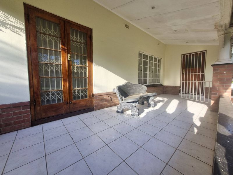A covered patio area featuring tiled flooring, brick accents, and secure wooden french doors leading into the home.